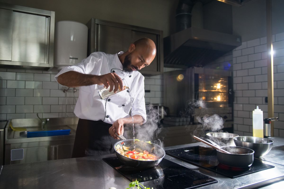 Chef adding spices to a dish in a commercial kitchen