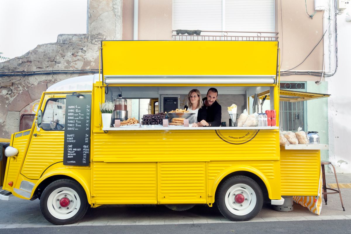 Yellow food truck with two people inside selling premium waffles using waffle maker